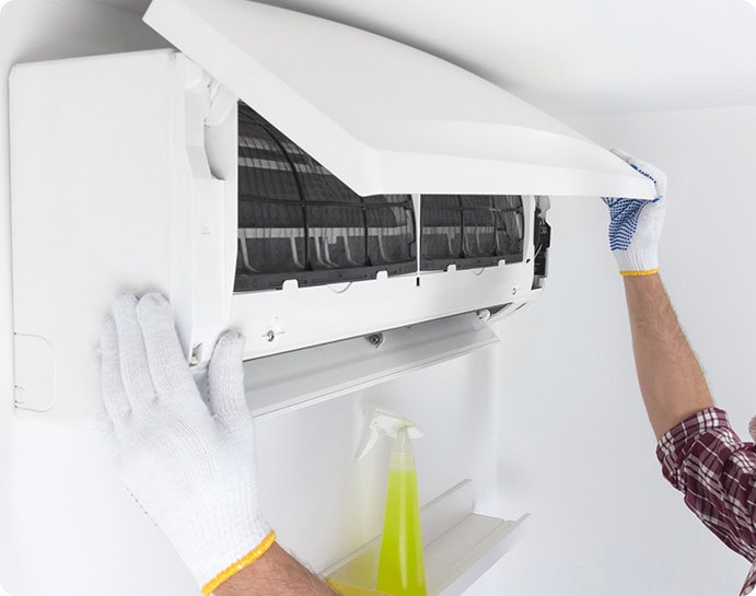 Osoba w białych rękawiczkach skrupulatnie reguluje przedni panel klimatyzatora zamontowanego na ścianie. Żółta butelka ze spryskiwaczem do czyszczenia wygodnie stoi na pobliskiej półce.